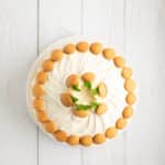 A banana pudding layer cake topped with swirled white frosting, surrounded by a ring of vanilla wafer cookies, and garnished with a few mint leaves in the center.