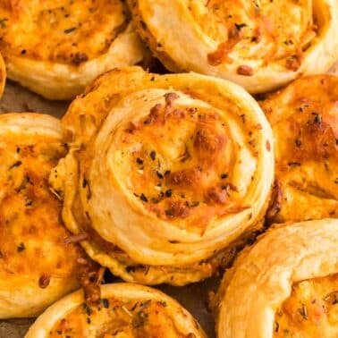 A close-up of several golden-brown buffalo chicken pinwheels on parchment paper.