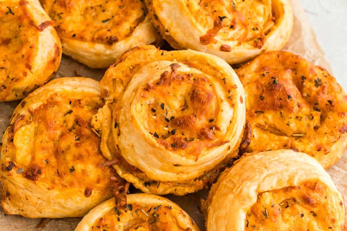A close-up of several golden-brown buffalo chicken pinwheels on parchment paper.