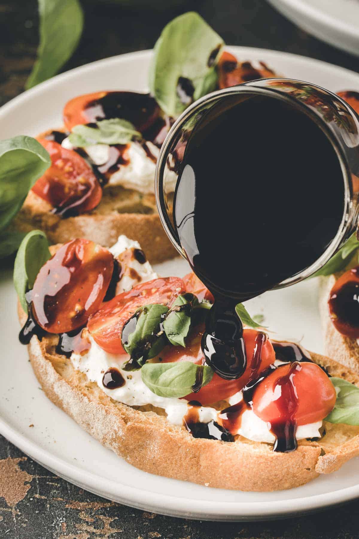 A close-up of caprese garlic bread with tomatoes, basil, and cheese on bread, as balsamic glaze is being poured over the top.