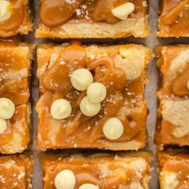 Close-up of caramel blondie bars topped with white chocolate chips and a sprinkle of sea salt, arranged in a grid pattern.