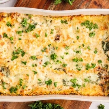 A baked spinach and chicken lasagna in a rectangular white dish, topped with melted cheese and chopped parsley.