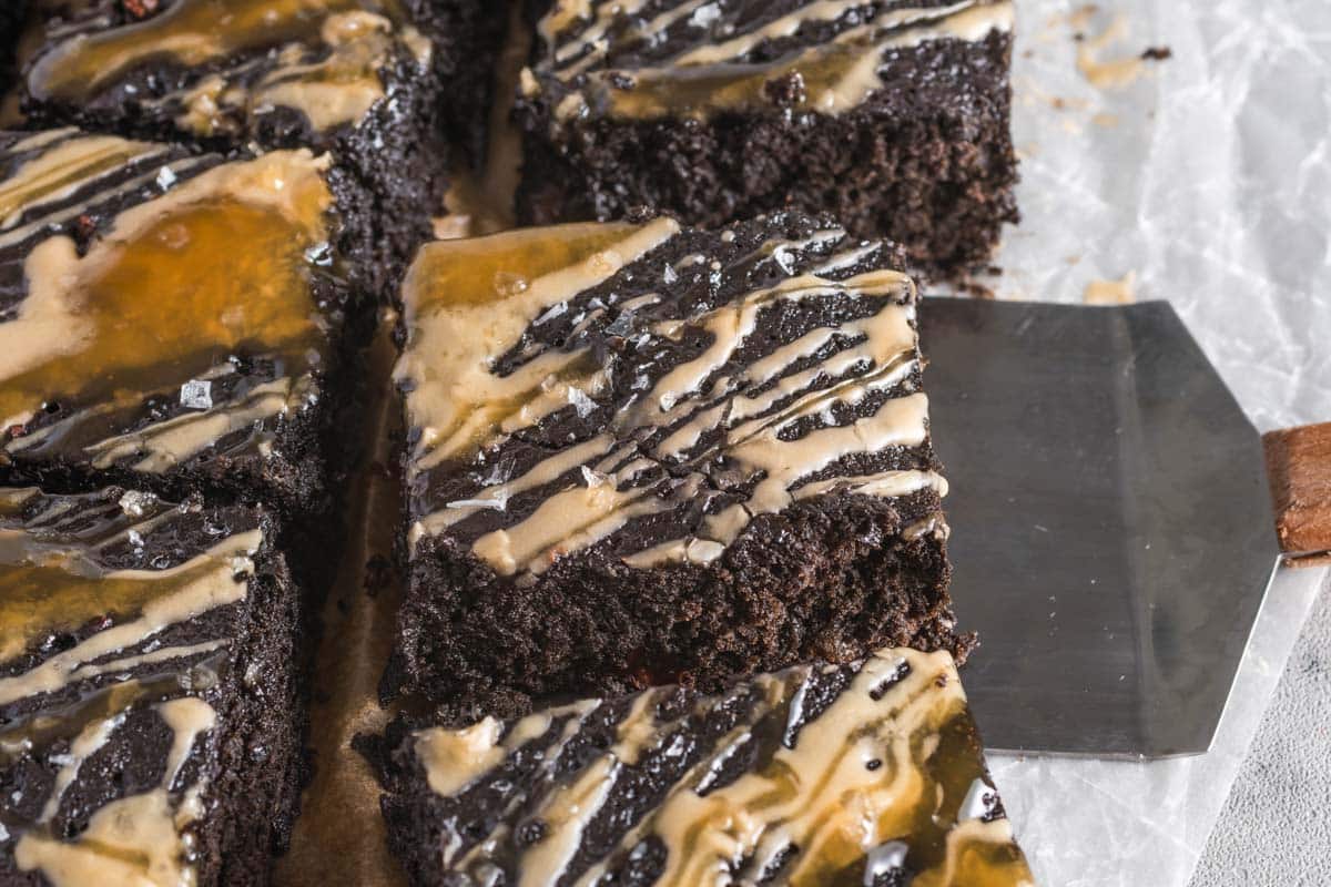 Close-up of sliced espresso brownies topped with a light caramel drizzle, arranged on parchment paper with a metal spatula beside them.