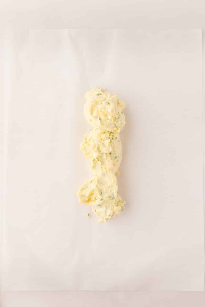 A mound of herbed butter is placed on a sheet of white parchment paper.