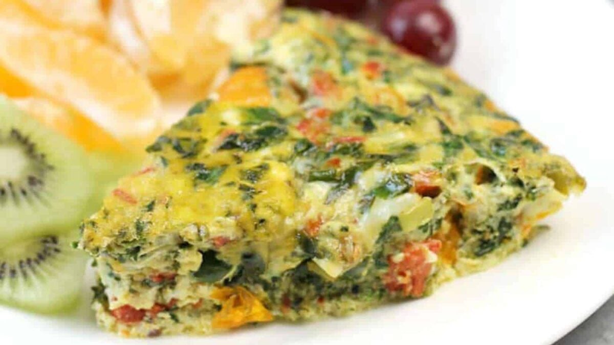 A slice of vegetable frittata on a plate, served with sliced kiwi, orange segments, and red grapes—perfect for anyone seeking fresh quiche ideas or inspiration for their next savory quiche.