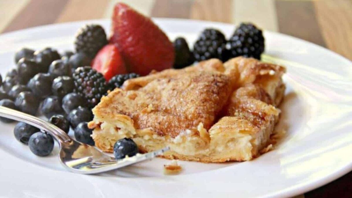A slice of baked pastry with a golden crust is served on a white plate with fresh blueberries, blackberries, and strawberries—perfect for those seeking sweet breakfast ideas. A fork rests on the plate.