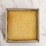 A square pan of plain, golden baked cake sits on a white marble surface with a white cloth partially visible at the bottom left.