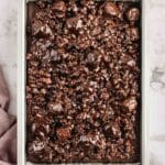 A rectangular metal baking pan filled with glossy, chocolate-covered clusters on a marble surface next to a mauve cloth.