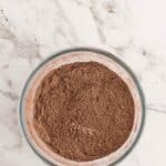A glass bowl filled with cocoa powder sits on a white marble surface.