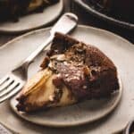 A slice of chocolate hazelnut cake topped with chopped nuts and pears on a gray plate, with a fork placed beside it.