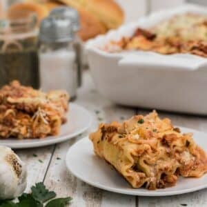 Two plates with lasagna rollups filled with cheese and sauce are on a table, with a baking dish of more lasagna in the background.