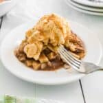 A slice of apple pie topped with a scoop of vanilla ice cream and caramel sauce on a white plate, with a fork resting on the dessert.