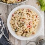 A white bowl filled with macaroni salad mixed with diced vegetables and a creamy dressing, placed on a wooden surface.