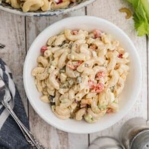 A white bowl filled with macaroni salad mixed with diced vegetables and a creamy dressing, placed on a wooden surface.