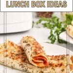 Two rolled flatbread sandwiches filled with meat and cheese are on a white plate, topped with herbs. Text overlay reads, "15 Back to School Lunch Box Ideas.