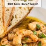 A bowl of shrimp in a sauce garnished with herbs, served with two slices of crusty bread. Text reads: "29 Seafood Recipes That Taste Like a Vacation.