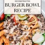 A bowl filled with ground beef, sliced cucumbers, cherry tomatoes, lettuce, pickles, French fries, crispy onions, and a drizzle of sauce; sauce cup shown in background.