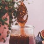 A spoon drips fig syrup into a glass jar, with a fig and a potted plant in the background. The text reads "Easy Fig Syrup" and "southernfoodandfun.com.