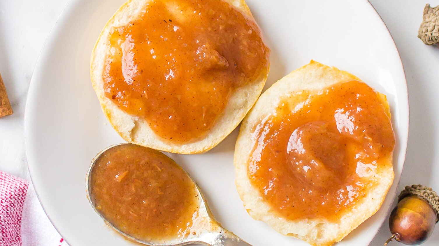Two biscuit halves with slow cooker apple butter spread on a white plate, next to a spoon with more jam.