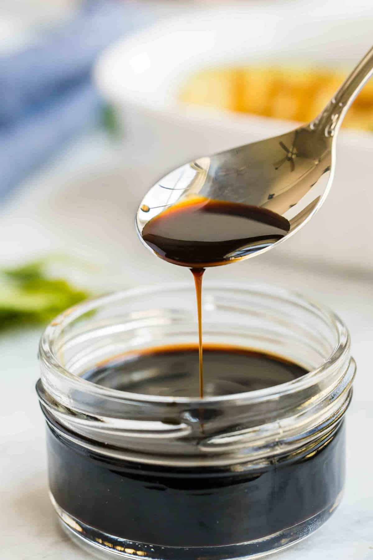 A spoon drizzling balsamic vinegar reduction into a small glass jar filled with a thick, black sauce.