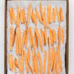 A baking sheet lined with parchment paper holds evenly spaced, uncooked sweet potato fries arranged in rows, ready for baking.