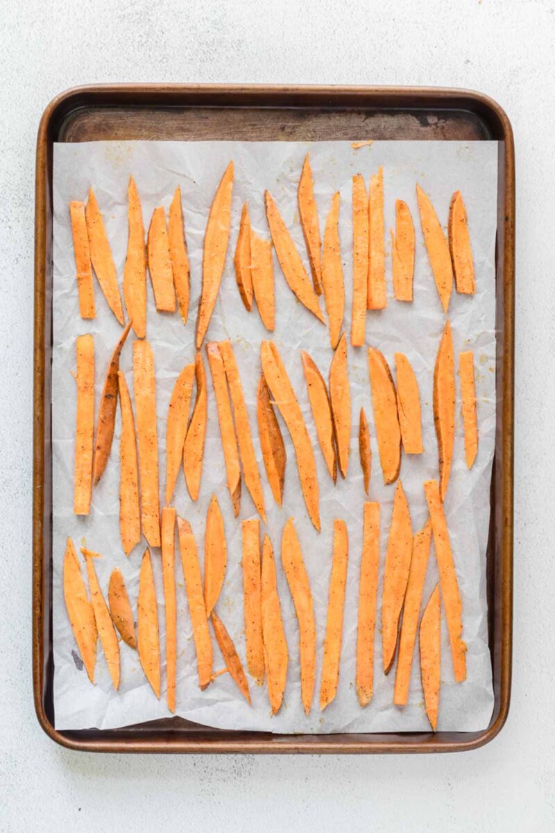 A baking sheet lined with parchment paper holds evenly spaced, uncooked sweet potato fries arranged in rows, ready for baking.