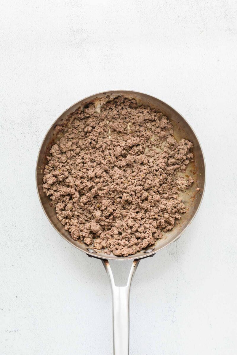A stainless steel pan filled with cooked and crumbled ground beef on a white surface.