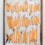 A baking tray lined with parchment paper holds evenly spaced, baked sweet potato fries.