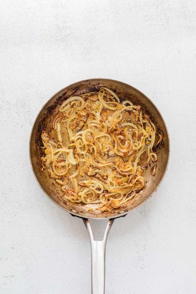 A stainless steel pan filled with sautéed, browned onions sits on a light-colored surface.