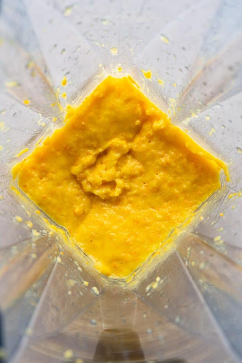 A close-up view of a blender containing a thick, yellow-orange mixture with some chunky texture.