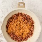 Ground beef cooking in a white skillet with taco seasoning sprinkled on top, viewed from above.