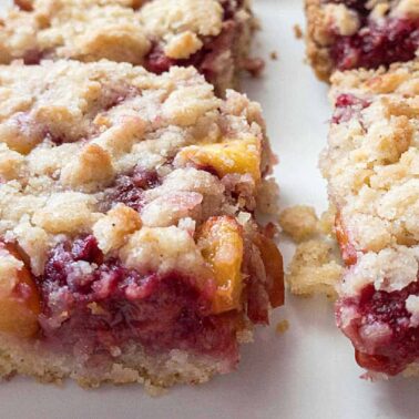 Close-up of fruit crumble bars with a golden crumb topping and a filling of mixed berries and peach pieces—an irresistible treat for fans of fresh fruit desserts.
