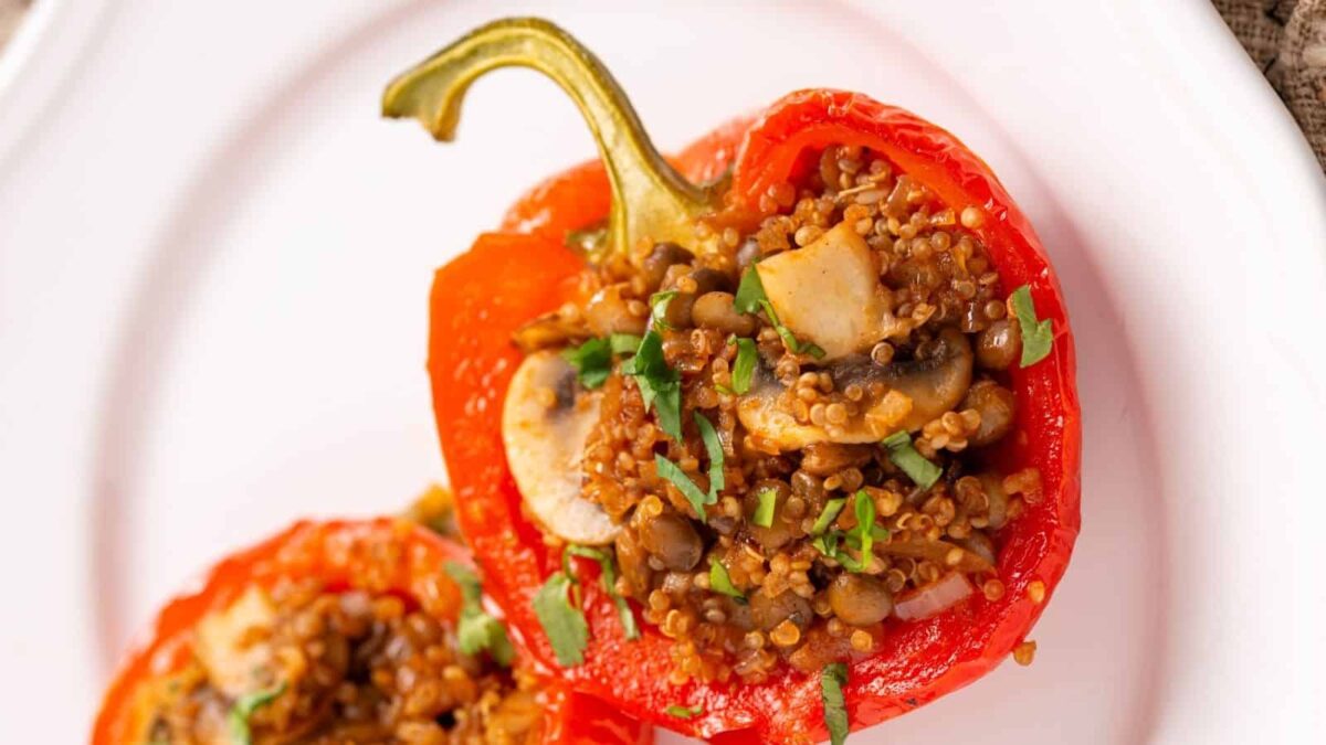A red bell pepper half stuffed with quinoa, mushrooms, lentils, and chopped herbs, served on a white plate—a delicious addition to your favorite stuffed pepper recipes.