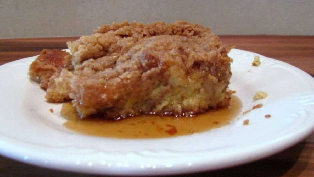A slice of cinnamon crumb cake sits on a white plate with syrup pooled underneath, making it a delightful addition to your collection of breakfast recipes.