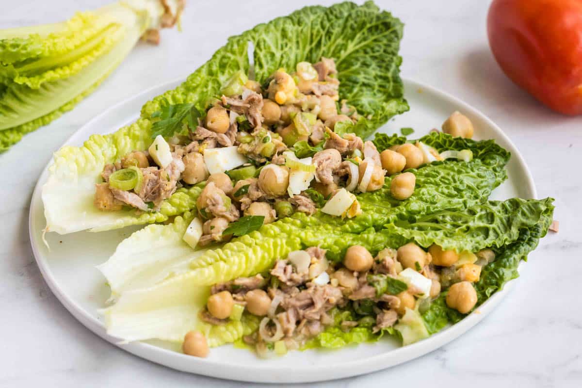 Romaine lettuce leaves topped with a mixture of canned chickpeas, tuna, chopped eggs, and green onions, served on a white plate—perfect for easy chickpea meals.
