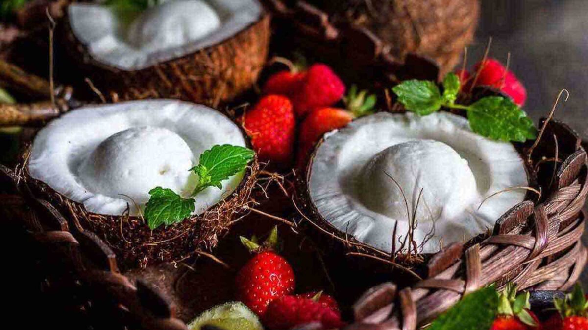 Two coconut shells filled with coconut ice cream, garnished with mint leaves, surrounded by fresh strawberries and mint on a woven surface—perfect for refreshing after-school treats or indulgent desserts.