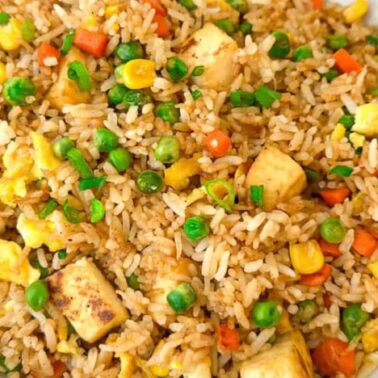 A close-up of a bowl of fried rice with peas, carrots, corn, tofu, scrambled egg, and chopped green onions—perfect for cozy autumn recipes and comforting fall dinners.