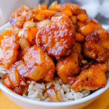 A bowl of white rice topped with glazed chicken pieces, diced orange bell peppers, and onions—perfect for easy dinner ideas and those who love comfort recipes.