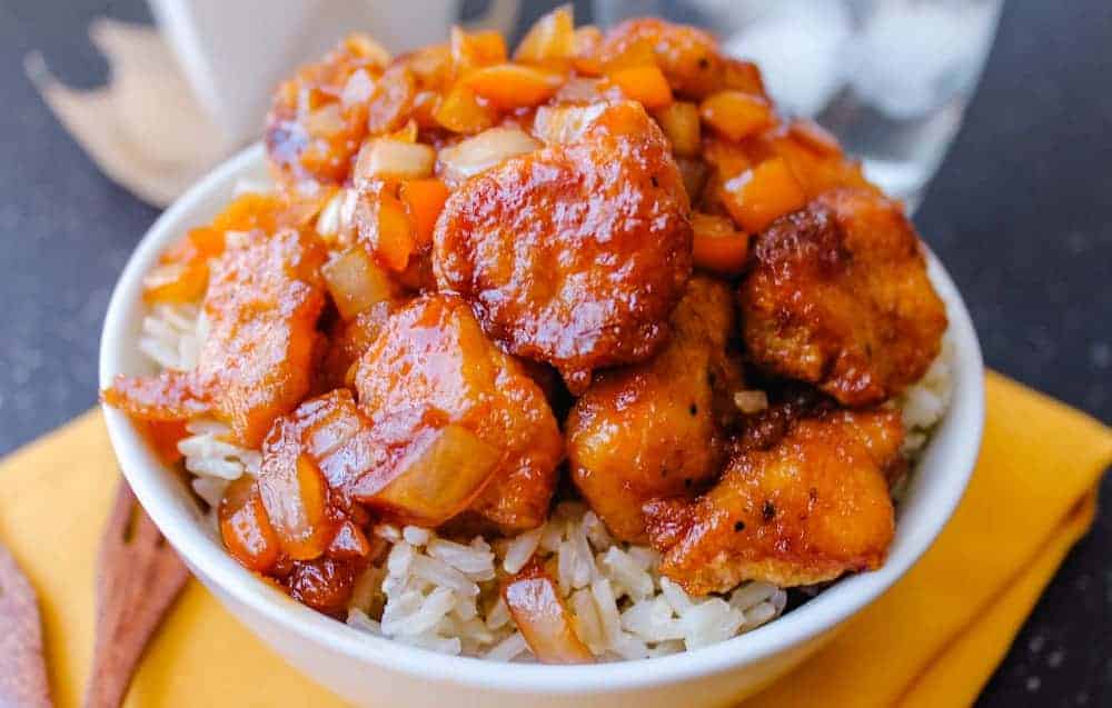 A bowl of white rice topped with glazed chicken pieces, diced orange bell peppers, and onions—perfect for easy dinner ideas and those who love comfort recipes.