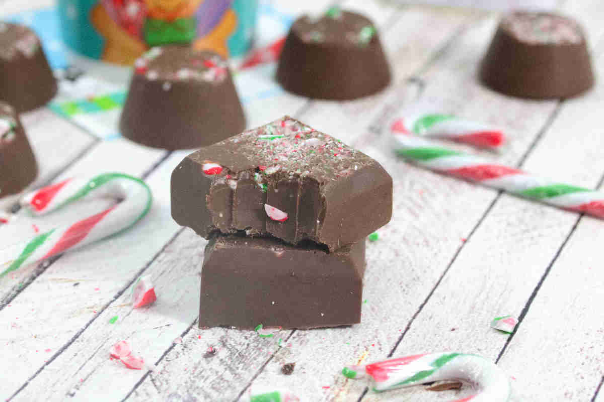 Two chocolate candies, one with a bite taken out, are stacked among broken pieces of candy canes on a white wooden surface—perfect inspiration for easy desserts and festive no-bake recipes.