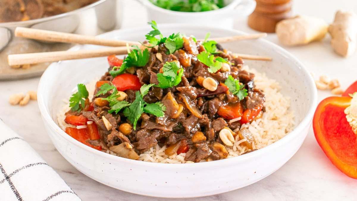 A bowl of rice topped with stir-fried beef, red bell pepper, onions, peanuts, and fresh cilantro—an ideal choice for simple meals with easy cleanup. Chopsticks rest on the bowl, ready for a quick and delicious experience.