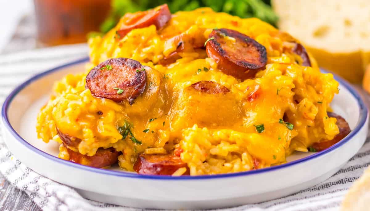A plate of cheesy rice topped with sliced sausage and herbs, served on a white plate with a blue rim—perfect for pork dinners or anyone looking for new dinner ideas.