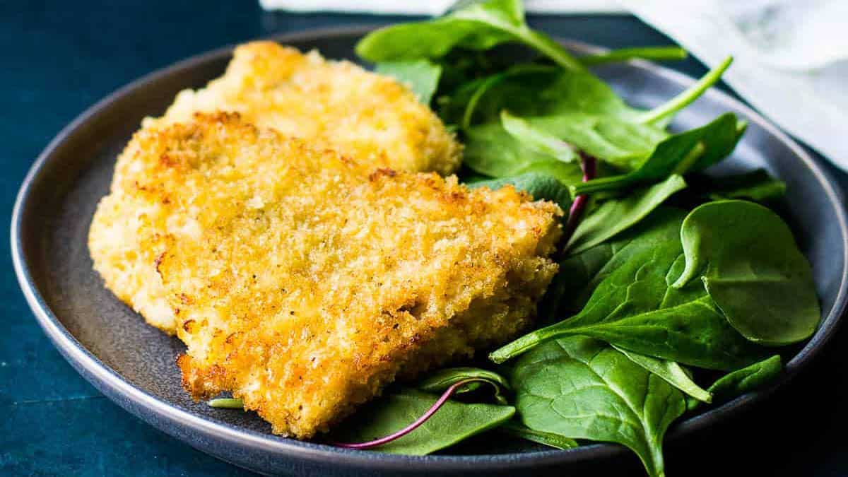 A plate with breaded and fried chicken cutlets next to a serving of fresh spinach leaves—perfect for easy dinners on busy weeknights.