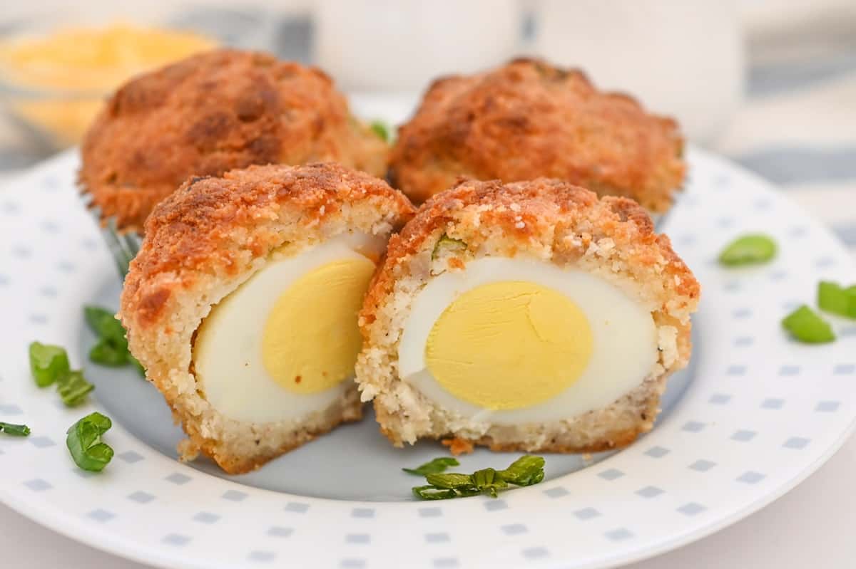 A halved Scotch egg with a visible hard-boiled egg center wrapped in seasoned sausage meat and breadcrumb coating, served on a white plate with green garnish—perfect for kids breakfast or creative school breakfast ideas.