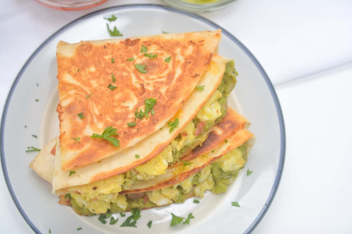 Two folded quesadillas filled with egg and green vegetables, garnished with chopped parsley, served on a white plate—perfect for easy school breakfasts and quick kids breakfast recipes.