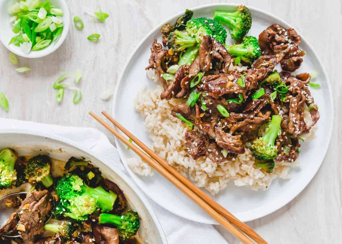 A plate of beef and broccoli stir-fry served over rice, garnished with sliced green onions, with a pair of wooden chopsticks on the side—perfect for easy stir-fry weeknight meals.