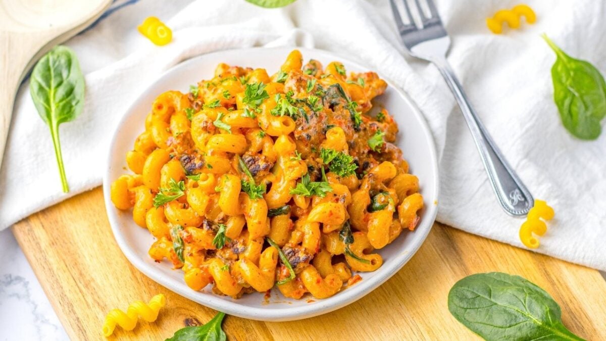 A white bowl filled with cooked macaroni pasta mixed with sauce, herbs, and garnished with chopped parsley offers a fresh twist on classic pasta dinners, beautifully presented on a wooden board.