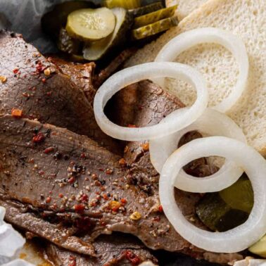 Sliced beef brisket topped with raw onion rings, served with pickle slices and two pieces of white bread—perfect for easy dinners that taste like impressive meals.