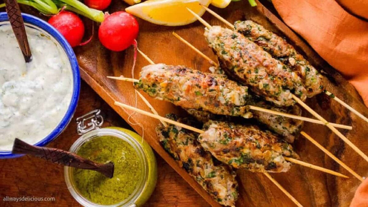 Grilled meat skewers served on a wooden platter with sauce, green dip, whole radishes, and lemon wedges—perfect for easy dinner ideas or anyone seeking inspiration for baked dinners and oven recipes.