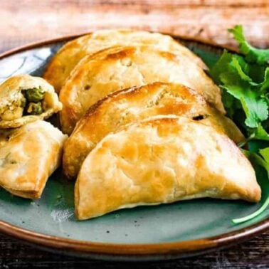A plate with five baked empanadas, one cut open to reveal a vegetable filling, garnished with fresh cilantro—perfect for those seeking new baked dinner recipes.